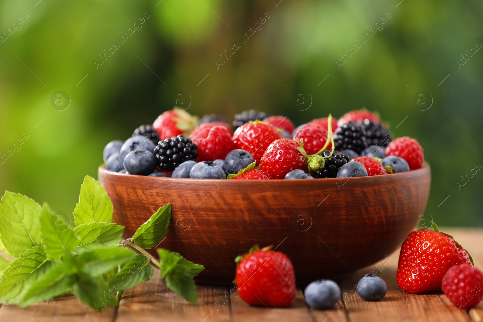 Photo of Bowl with different fresh ripe berries and mint on wooden table outdoors