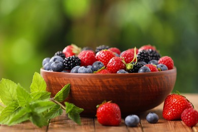 Bowl with different fresh ripe berries and mint on wooden table outdoors