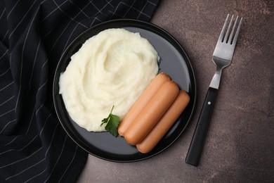 Photo of Delicious boiled sausages, mashed potato, parsley and fork on brown table, top view