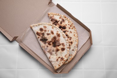 Photo of Tasty pizza calzones on white tiled table, top view