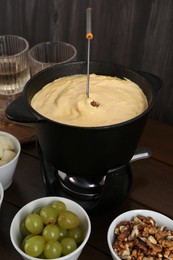 Photo of Fondue pot with tasty melted cheese, fork and different snacks on wooden table