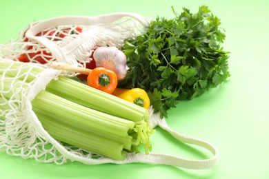 Photo of String bag with different vegetables on light green background, closeup
