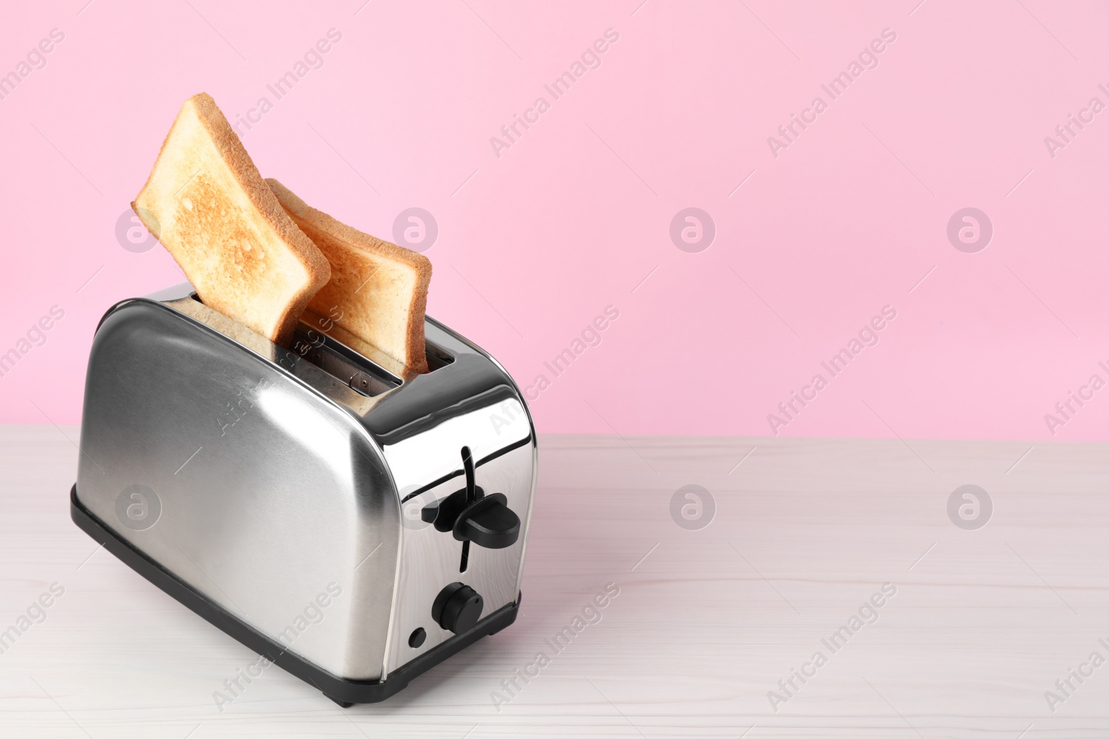 Photo of Modern toaster with slices of bread on white wooden table. Space for text