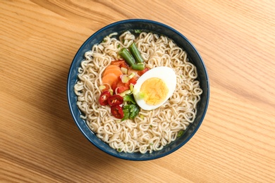 Bowl of noodles with broth, egg and vegetables on wooden background, top view