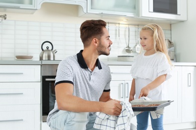 Young man treating his daughter with homemade oven baked baked cookies in kitchen