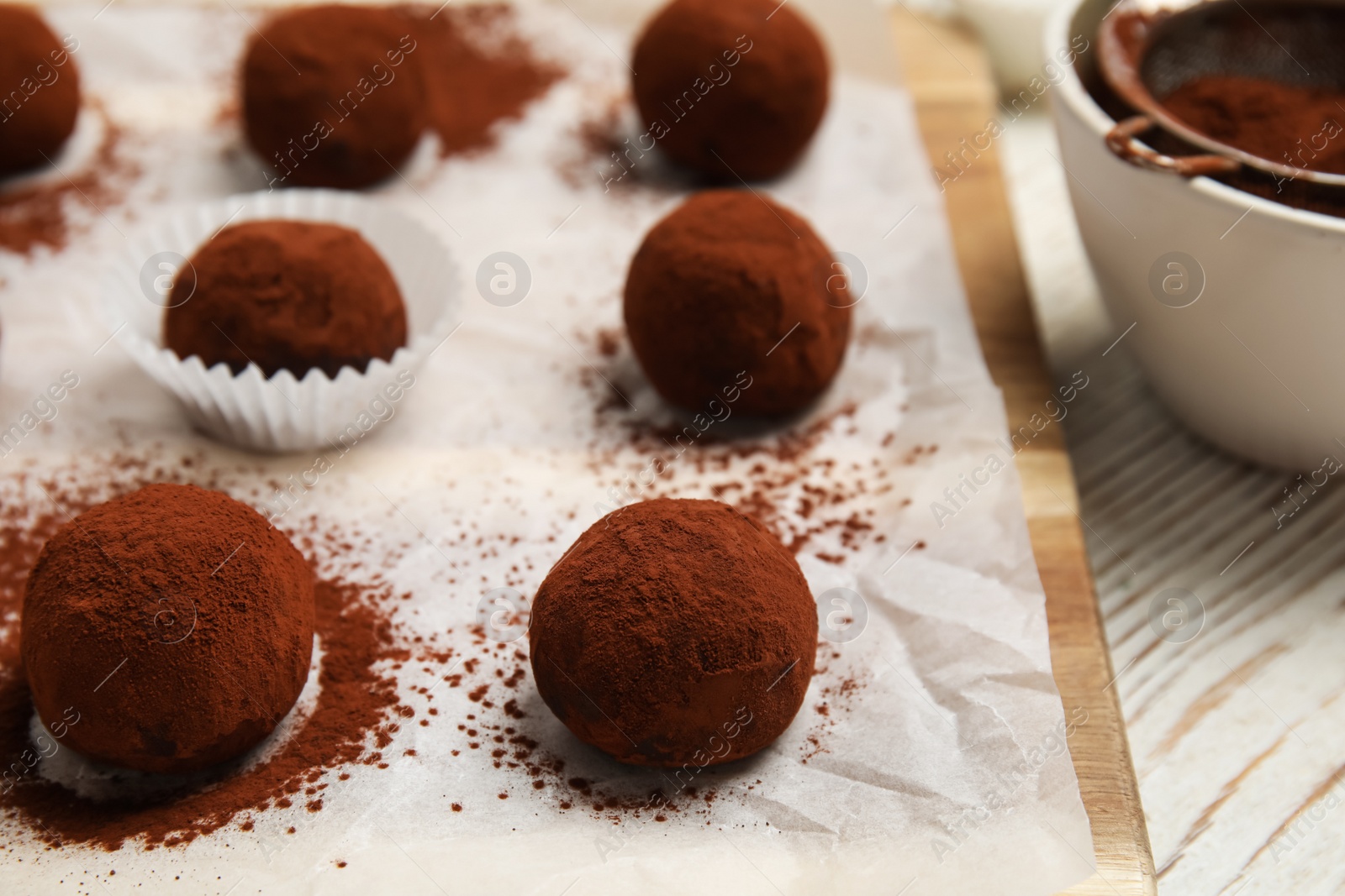 Photo of Delicious chocolate truffles powdered with cocoa on white wooden table, closeup