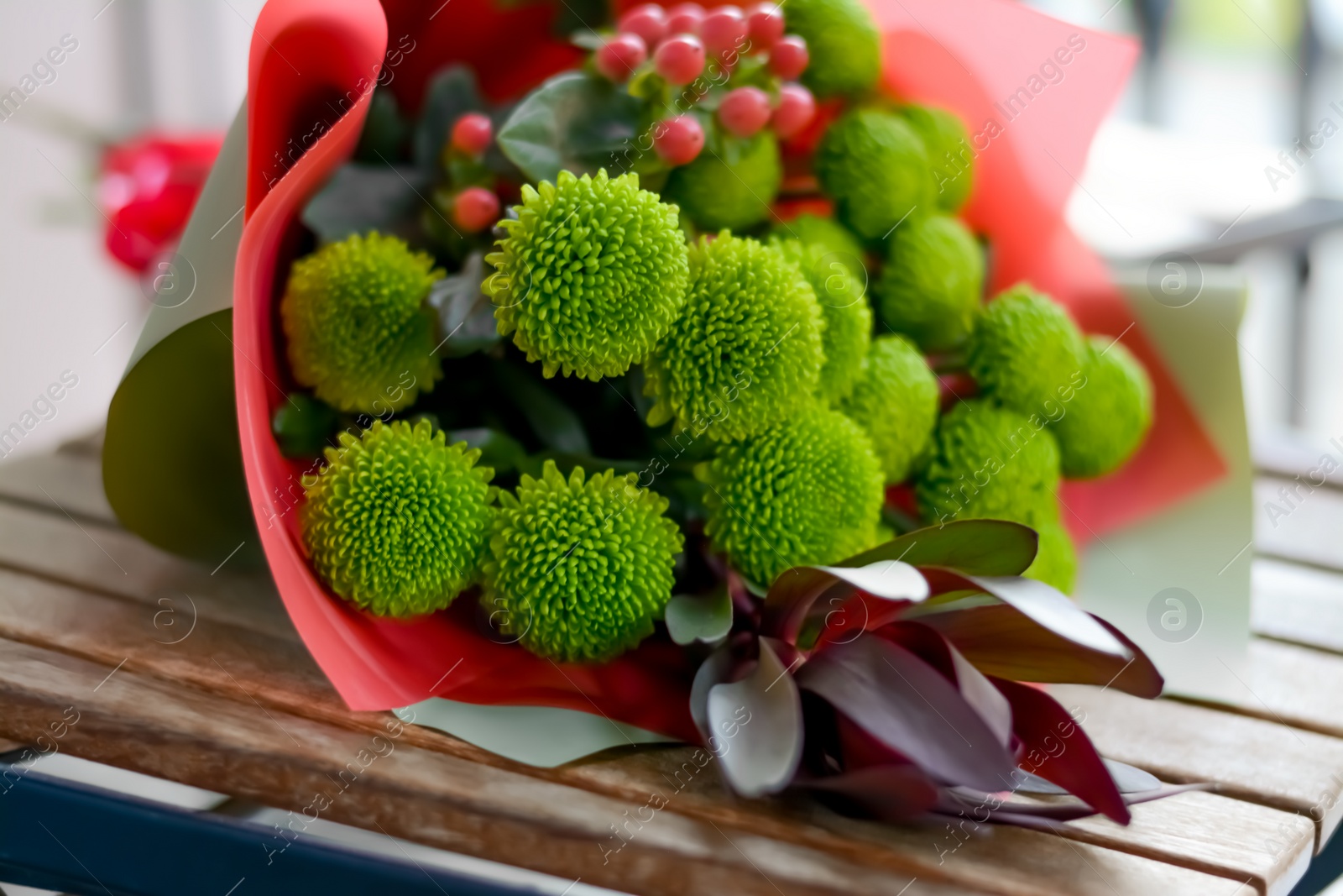 Photo of Bouquet of beautiful flowers wrapped in paper on wooden table, closeup