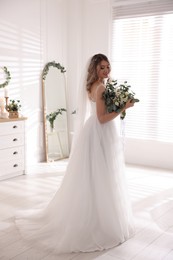 Photo of Happy bride wearing beautiful wedding dress with bouquet at home