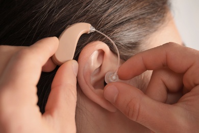 Doctor putting hearing aid in patient's ear, closeup