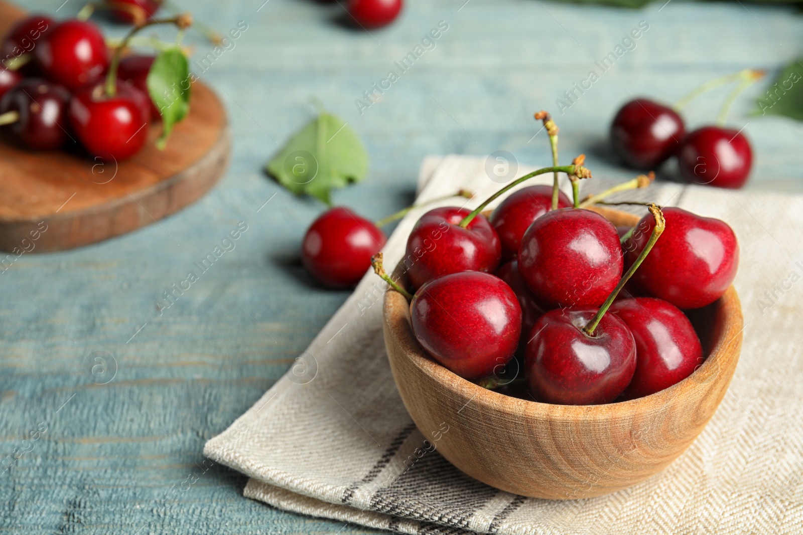 Photo of Wooden bowl with ripe sweet cherries on light blue table. Space for text