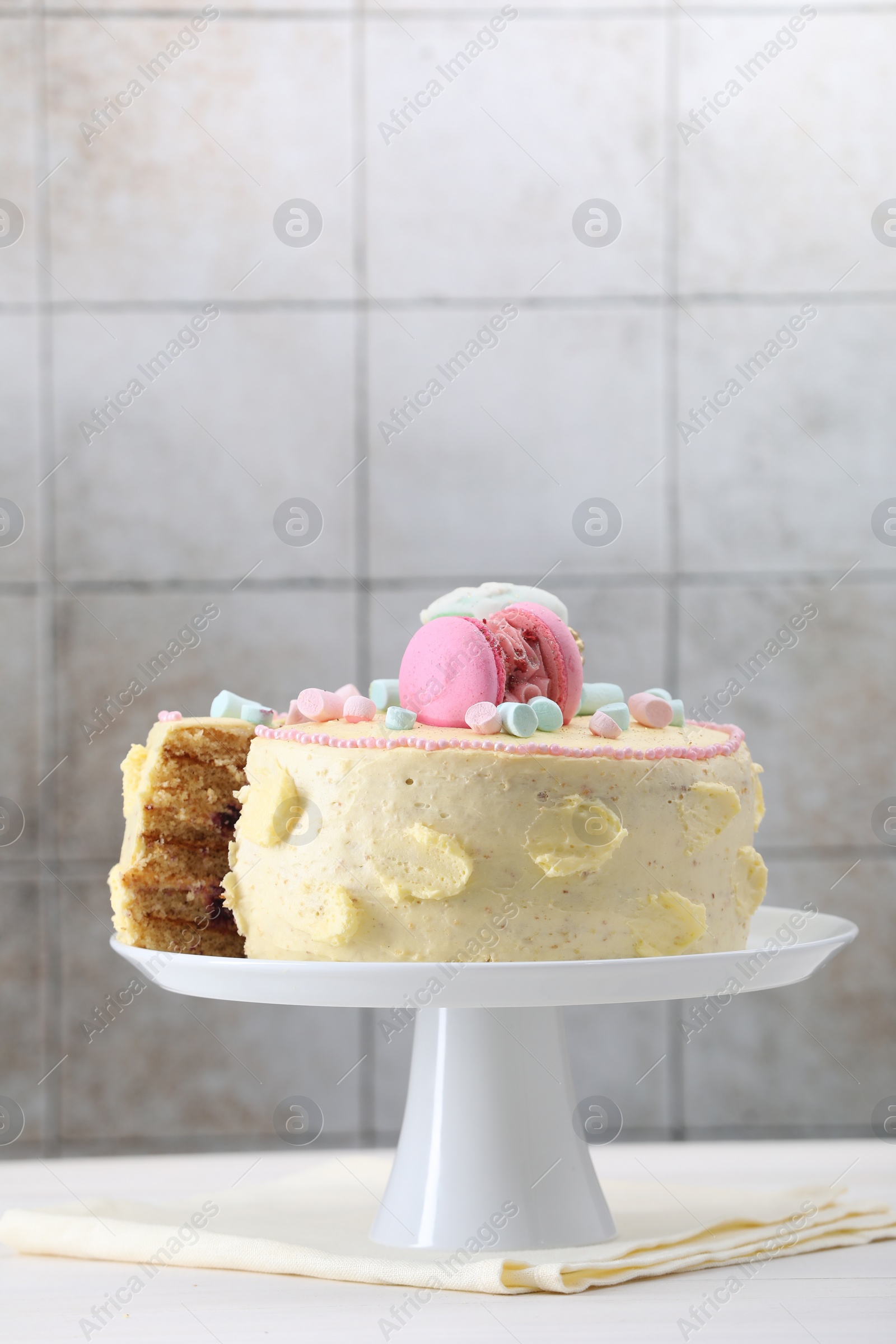 Photo of Delicious cake decorated with macarons and marshmallows on white table against tiled background, space for text