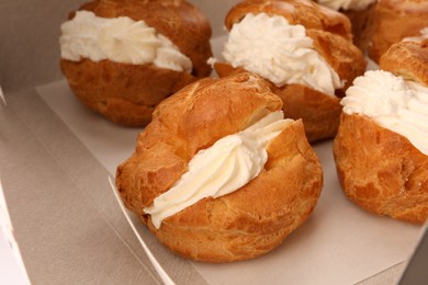 Delicious profiteroles with cream filling on table, closeup