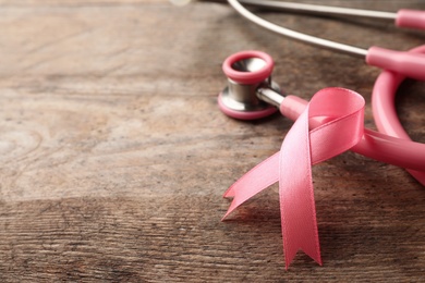 Photo of Pink ribbon and stethoscope on wooden background, space for text. Breast cancer concept