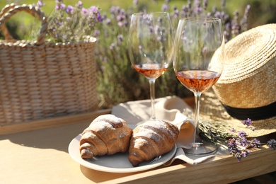 Photo of Plate with croissants and glasses of wine on wooden tray in lavender field