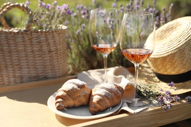 Plate with croissants and glasses of wine on wooden tray in lavender field