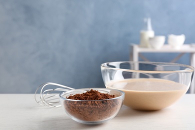 Photo of Glass bowls with cocoa powder and batter on white table in kitchen