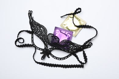 Photo of Lace mask and condoms on white background, top view. Sex game