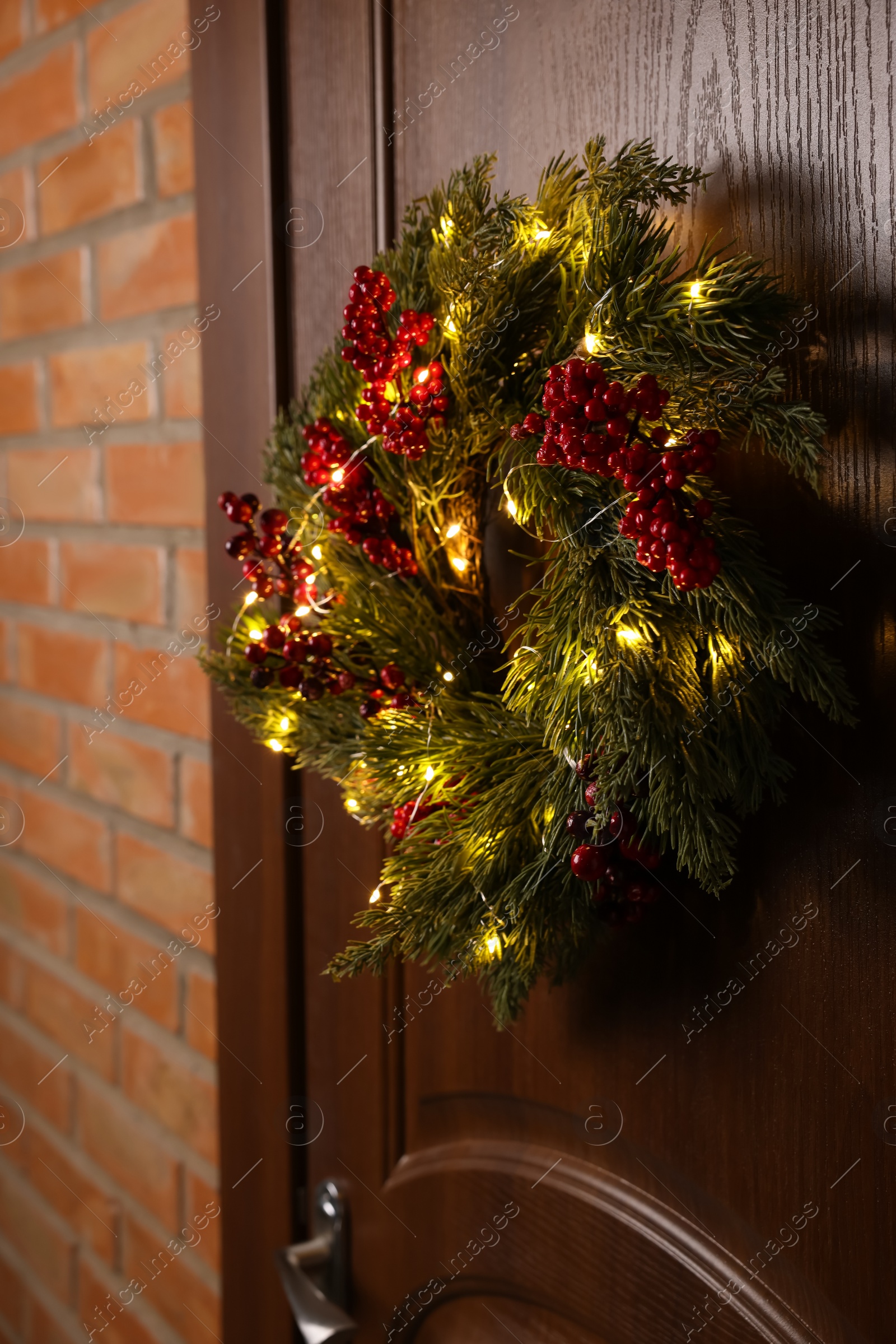 Photo of Beautiful Christmas wreath with red berries and fairy lights hanging on wooden door