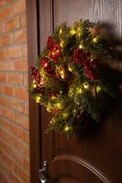 Beautiful Christmas wreath with red berries and fairy lights hanging on wooden door