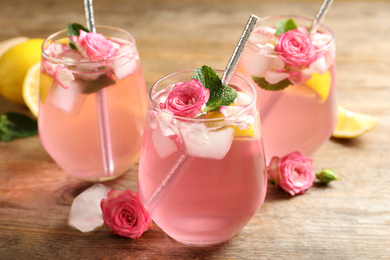 Delicious refreshing drink with rose flowers and lemon slices on wooden table, closeup