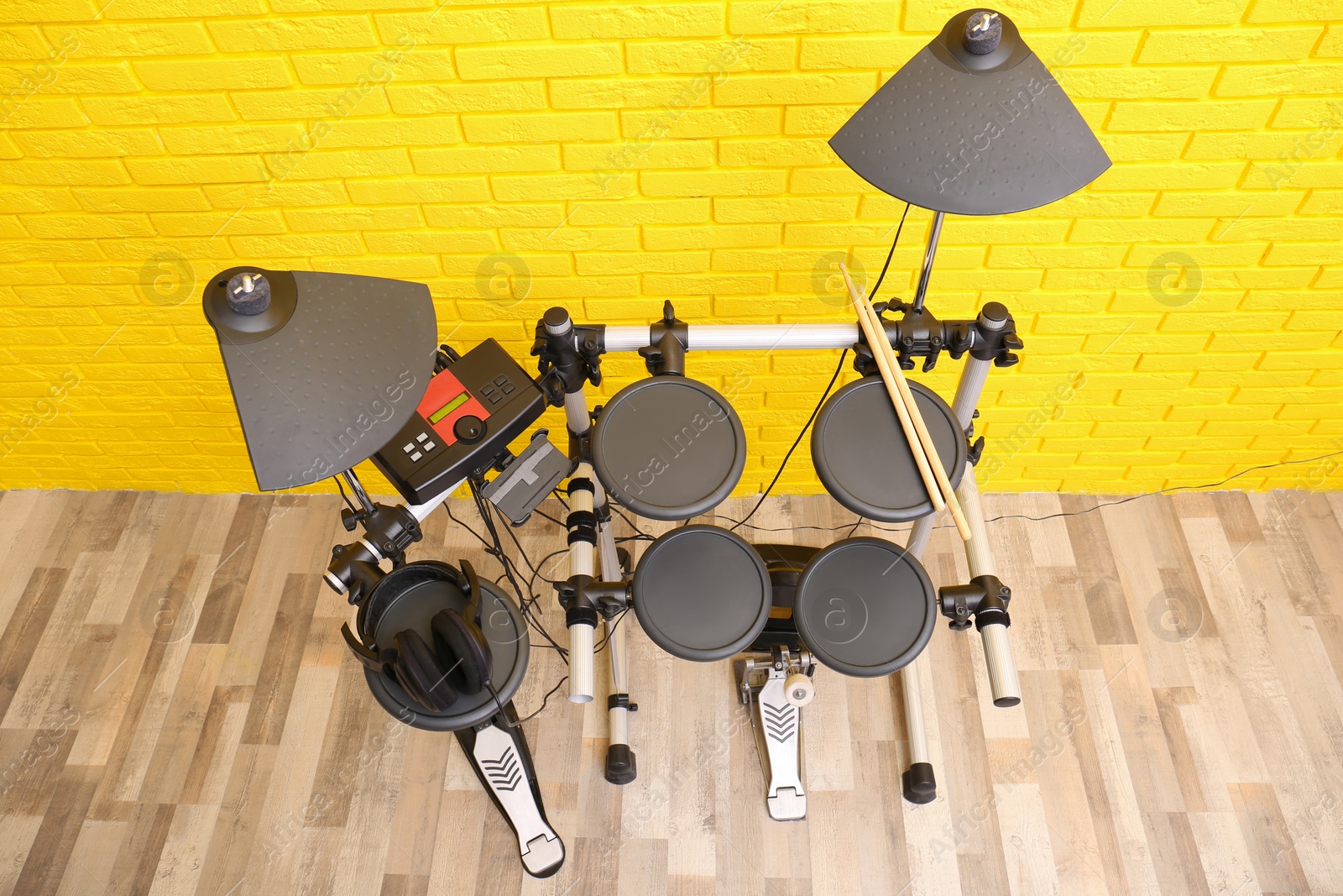 Photo of Modern electronic drum kit near yellow brick wall indoors, above view. Musical instrument