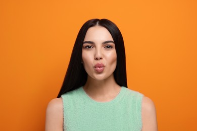 Beautiful young woman blowing kiss on orange background