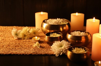 Photo of Tibetan singing bowls with beautiful flowers and burning candles on wooden table, space for text