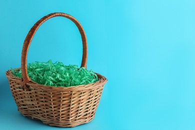 Photo of Easter basket with green paper filler on light blue background, space for text