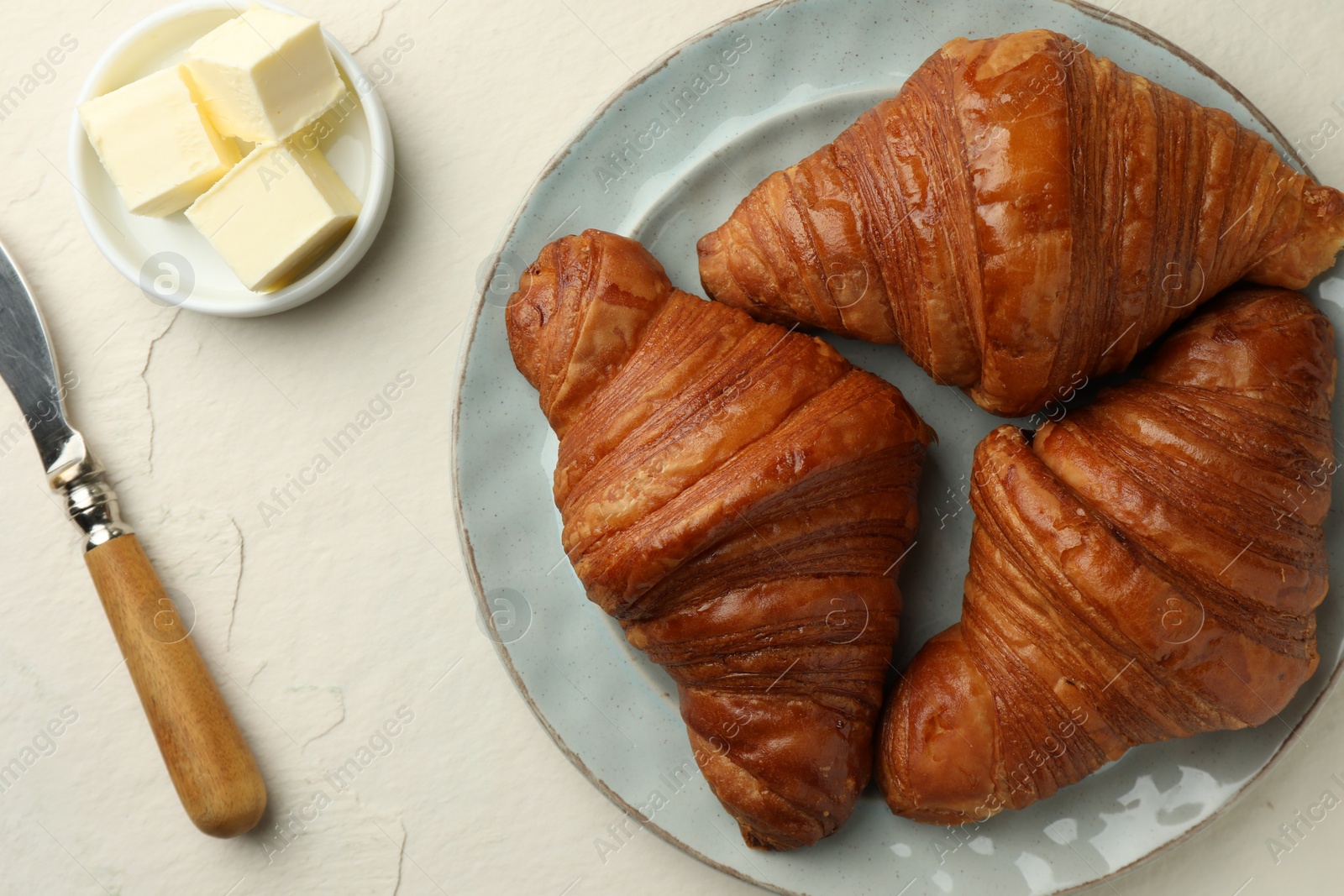 Photo of Plate with tasty croissants served on light textured table, flat lay