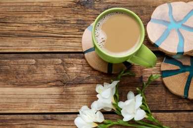 Mug of coffee, stylish cup coasters and beautiful freesia flowers on wooden table, flat lay. Space for text