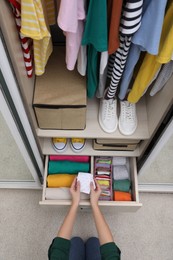 Photo of Woman folding clothes in wardrobe drawer indoors, top view. Vertical storage