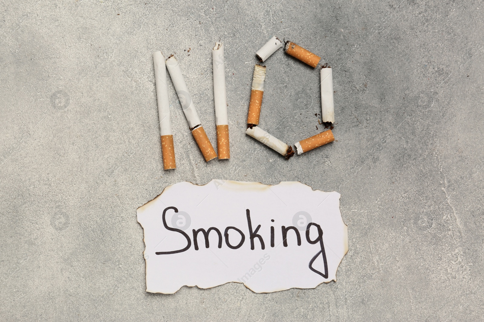 Photo of Words No Smoking made with cigarettes and paper on grey table, flat lay