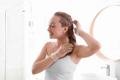 Photo of Young woman dyeing her hair in bathroom