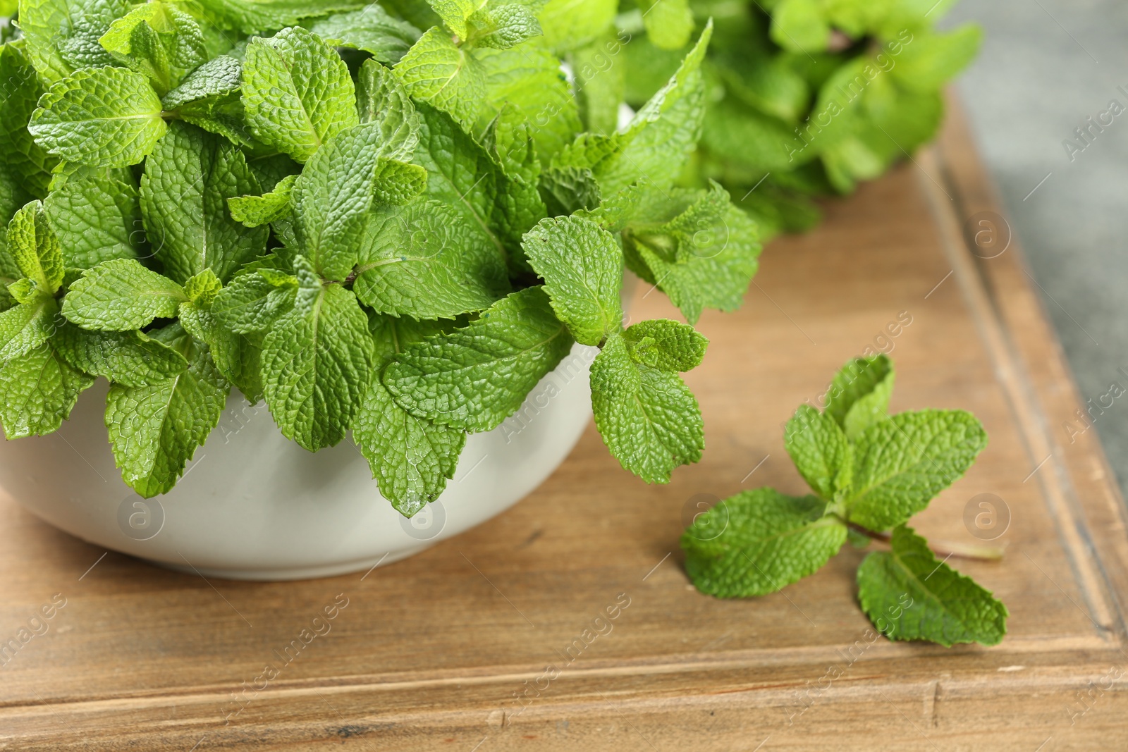 Photo of Bowl with fresh green mint leaves on wooden board, closeup