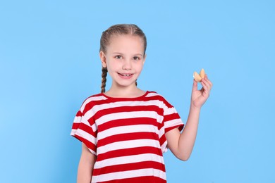 Cute girl holding tasty fortune cookie with prediction on light blue background