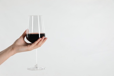 Woman holding glass of red wine on light background, closeup. Space for text