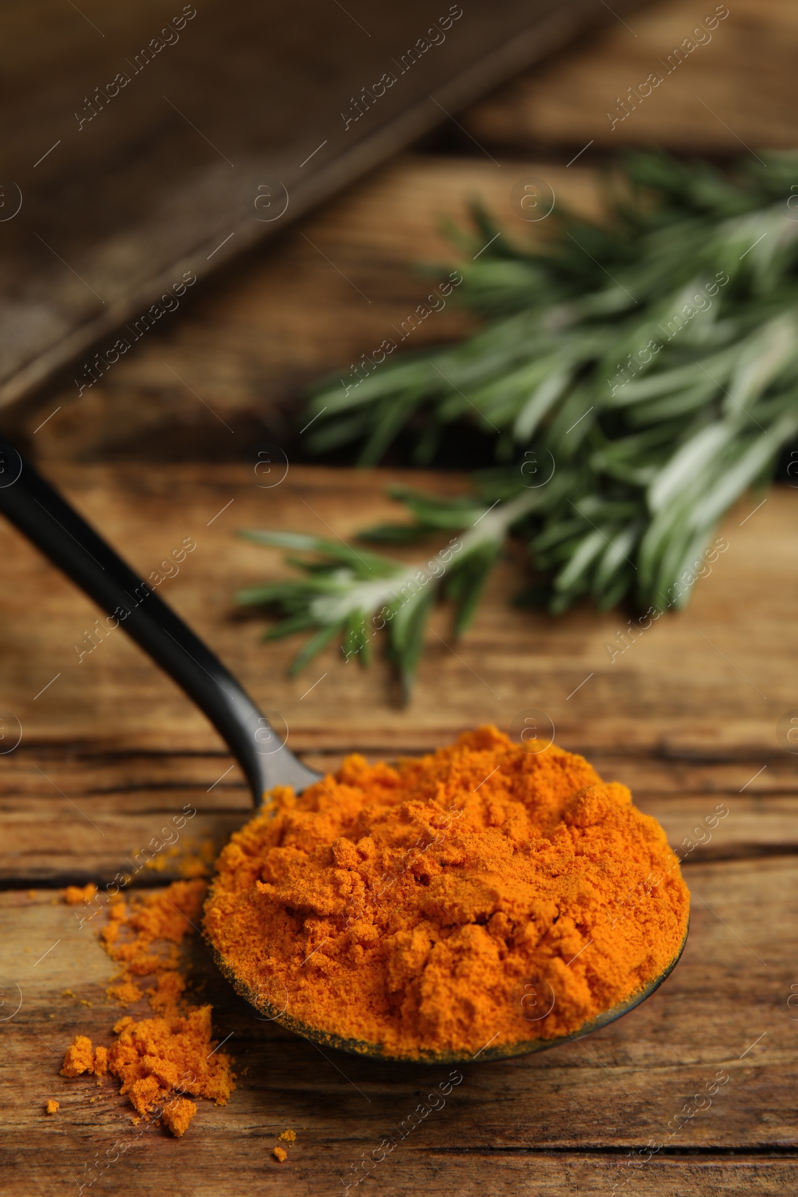 Photo of Spoon with saffron powder and rosemary on wooden table