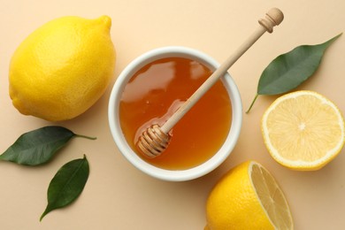 Ripe lemons, leaves, bowl of honey and dipper on beige background, flat lay