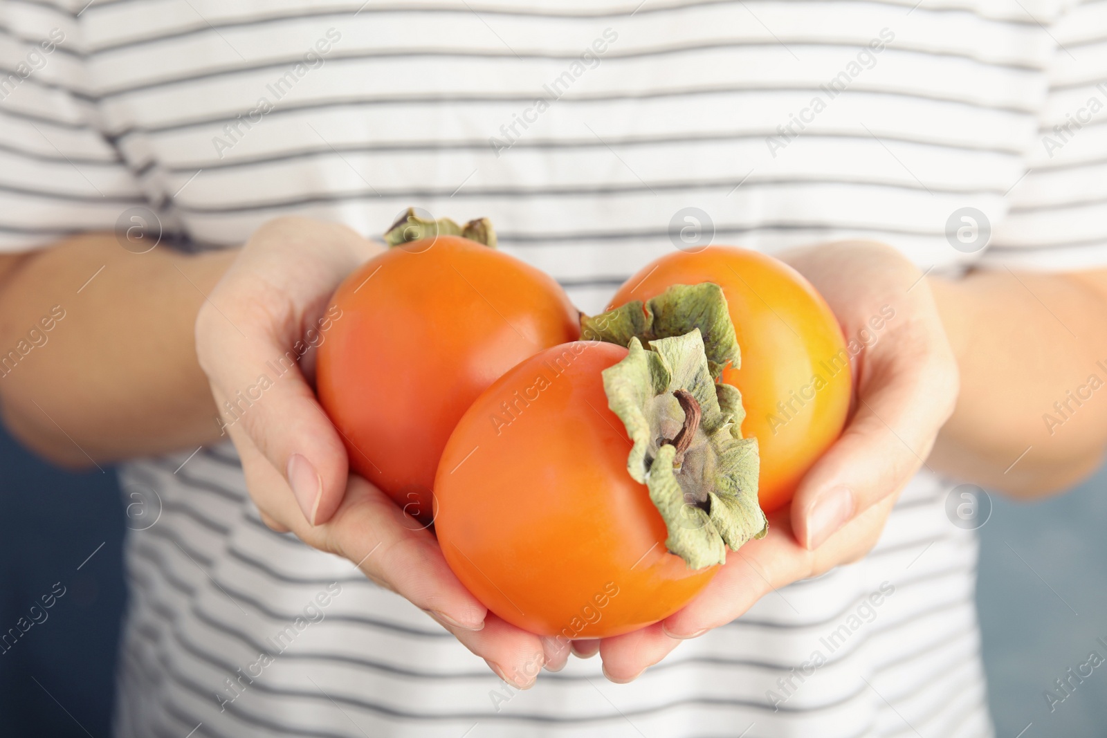 Photo of Woman holding delicious fresh persimmon fruits, closeup