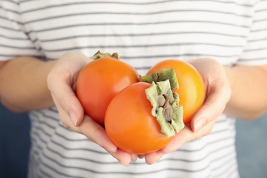 Photo of Woman holding delicious fresh persimmon fruits, closeup