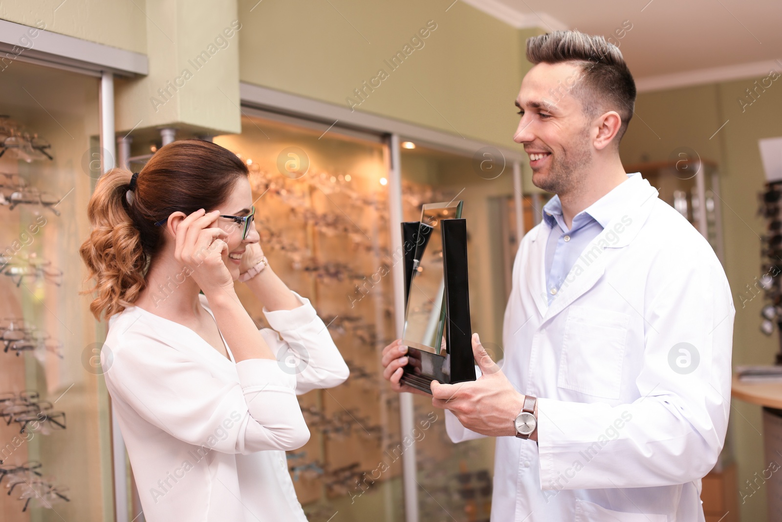 Photo of Male ophthalmologist helping woman to choose glasses in optical store