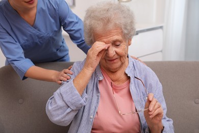 Photo of Nurse taking care of senior woman with headache indoors