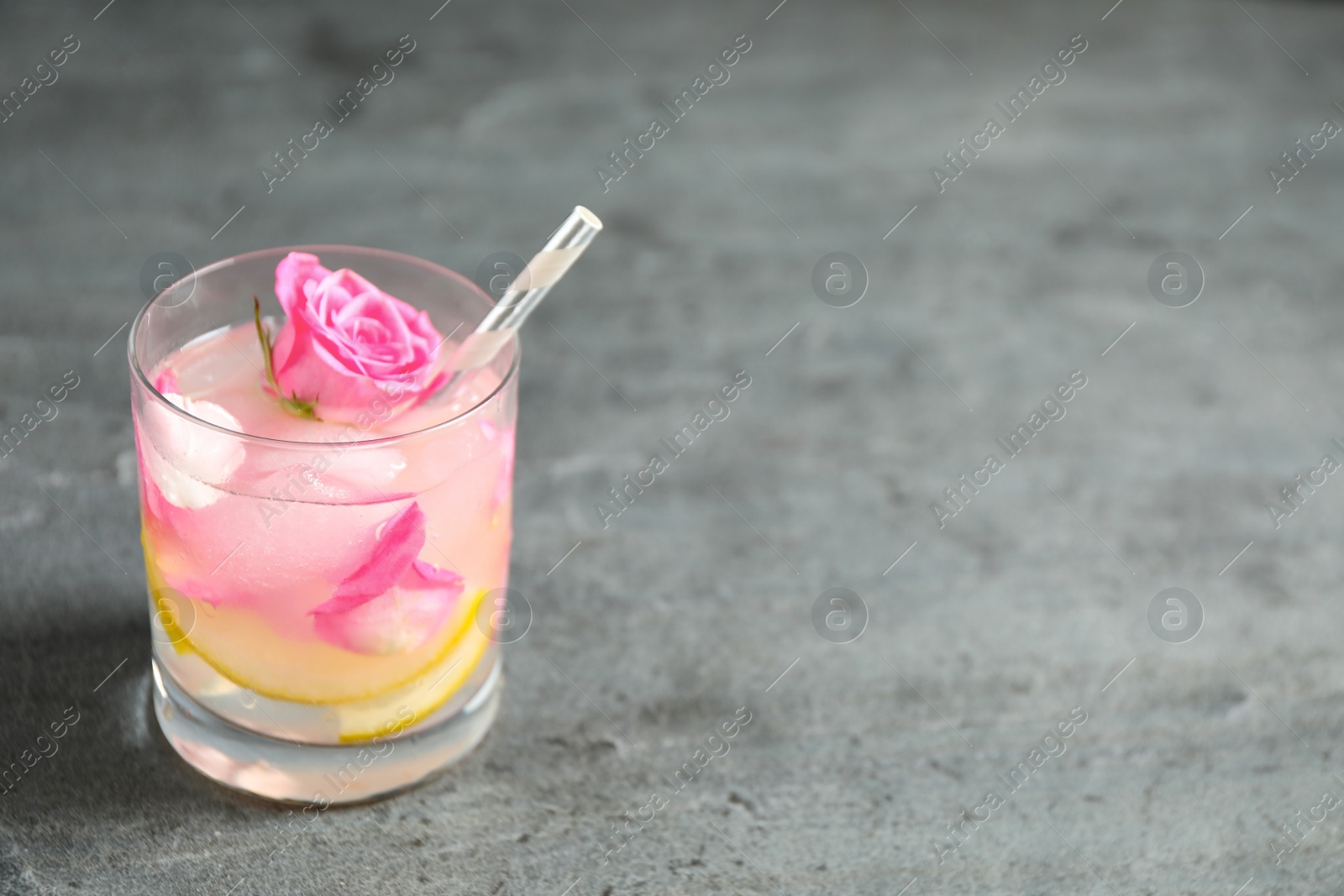 Photo of Glass of refreshing drink with lemon and roses on grey table. Space for text