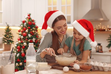 Mother with her cute little daughter making dough for Christmas cookies in kitchen