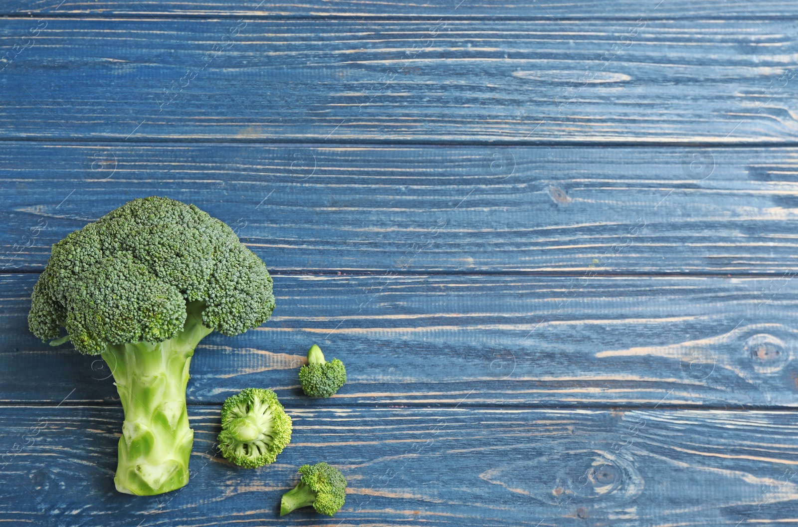 Photo of Fresh broccoli florets on blue wooden table, flat lay with space for text