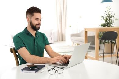 Photo of Handsome young man working with laptop at table in home office