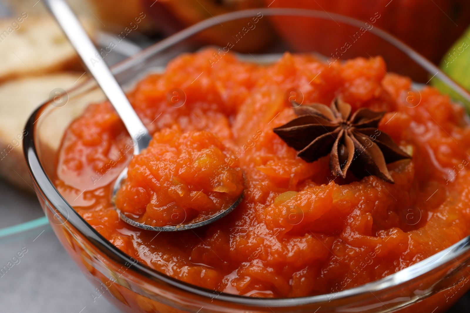 Photo of Bowl with delicious pumpkin jam, spoon and star anise on grey table, closeup