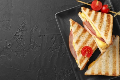 Photo of Tasty sandwiches with ham, melted cheese and tomatoes on black textured table, top view. Space for text