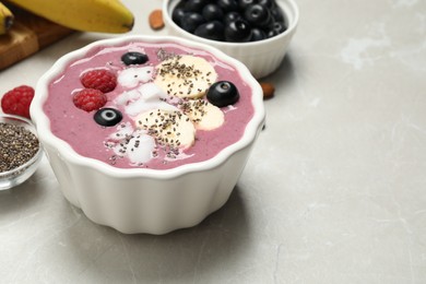 Photo of Delicious acai smoothie with fruits and coconut chips in dessert bowl on grey table. Space for text