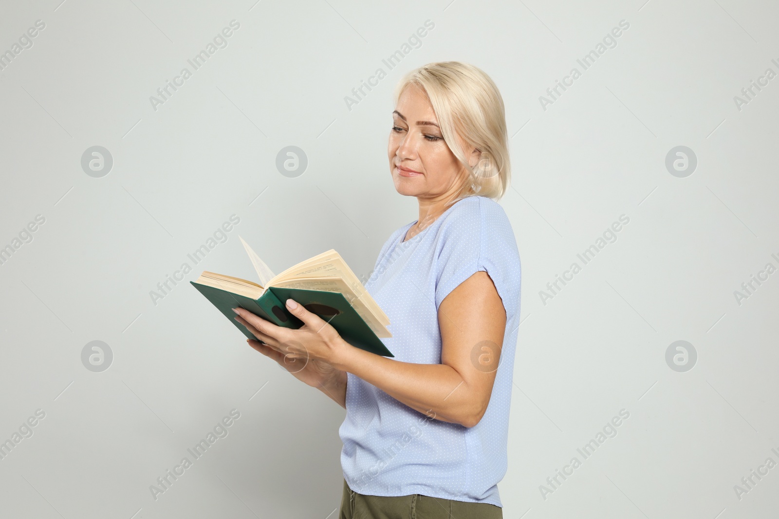 Photo of Mature woman reading book on light background